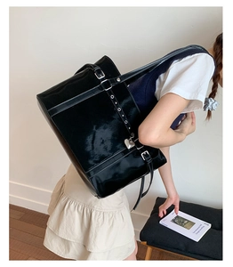 Detail of glossy black patent leather tote bag with silver metal eyelets and heart charm