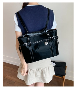 Detail of glossy black patent leather tote bag featuring silver heart pendant and buckle straps