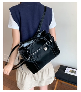 Detail of black glossy tote bag with silver buckles and heart charm shown on model