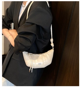 Detail of beige croissant shoulder bag featuring vertical stitching and metal logo on leather