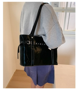 Detail of glossy black patent leather tote bag with silver metal buckle and long shoulder strap