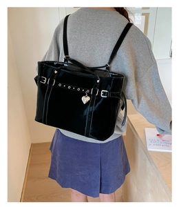 Detail of glossy black patent leather tote with silver heart charm on model's shoulder