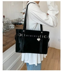 Close-up of black glossy tote bag with silver buckle strap and heart charm detail