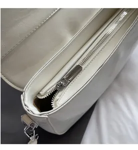 Detailed macro of smooth silver zipper and glossy wrinkled texture on white saddle bag