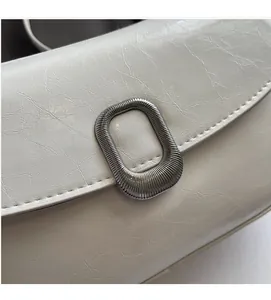 Close-up of white pleated leather bag featuring a silver metal oval buckle ornament