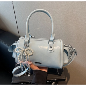 Detail of light blue Boston bag with pearl bow charm on black book background