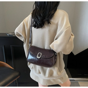 Detailed view of glossy dark brown leather crossbody bag with silver oval buckle hardware