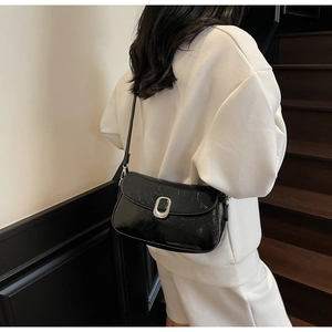 Glossy black underarm bag with silver oval buckle shown from a side-view on the shoulder