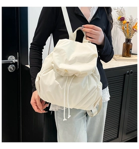 Close-up of minimalist cream pleated drawstring backpack styled on model in modern room
