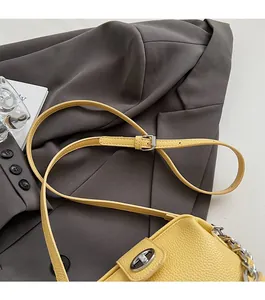 Close-up of yellow lychee grain leather handbag with silver chain and metal clasp detail