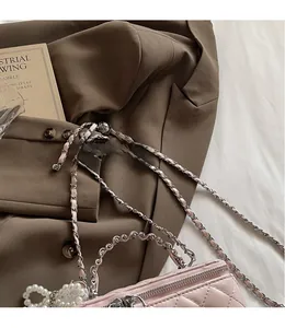 Close-up of pink quilted box bag with pearl lace charm and golden chain strap