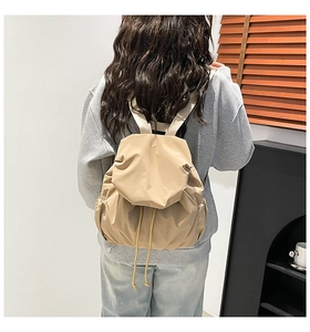 Woman wearing a beige pleated drawstring backpack in a minimalist indoor scene view