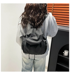 Rear view of a black drawstring nylon backpack showing size on a female model