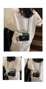 Detail of black quilted box bag with lace handle, pearls, and metal twist lock