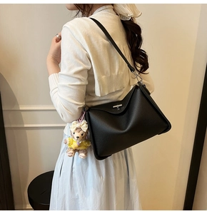 Detail of black pebbled leather Boston bag with silver twist lock and plush bear charm