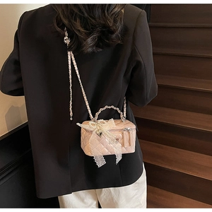 Pink quilted box bag featuring pearl handle and lace bow detail on a stylish model