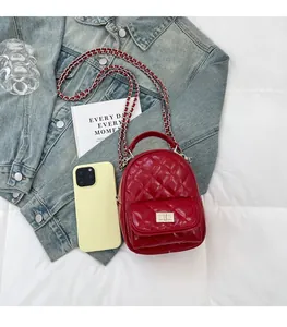 Mini red quilted leather backpack with silver chain strap shown next to a smartphone