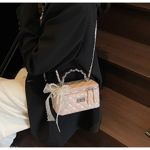 Detailed close-up of pink quilted patent leather box bag with pearl and lace bow charm
