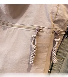 Detail of nylon tote bag featuring a woven rope zipper pull and smooth metal hardware