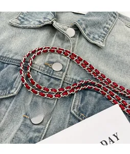 Detail of red leather interwoven with silver metal chain strap on denim fabric