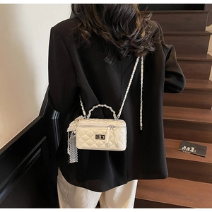 Detail of white quilted crossbody bag featuring metal buckle and pearl lace charm