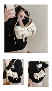 Dettaglio di una borsa sottobraccio a mezzaluna beige con due tasche frontali e fibbie