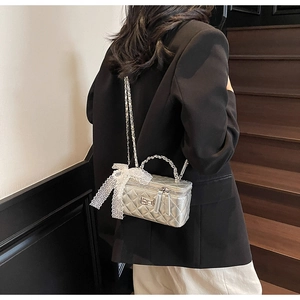 Detail of silver quilted mini box bag with lace bow and woven chain handle