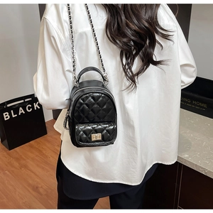 Close-up of black quilted mini backpack with silver chain strap worn by a model