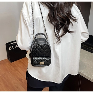 Detail of black quilted patent leather mini backpack with metal chain strap on model