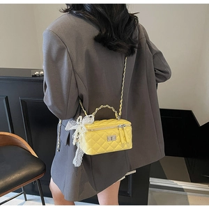 Detail of yellow quilted mini box bag with lace bow and pearl charm on a grey blazer