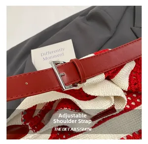 Detail of adjustable red leather shoulder strap with silver buckle on woven tote bag