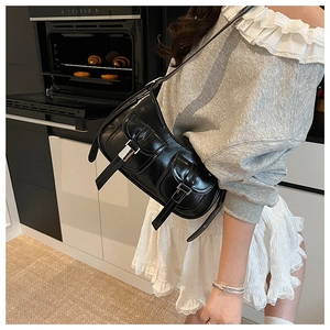 Dettaglio di una borsa a tracolla in pelle nera lucida con fibbie argentate in stile Y2K