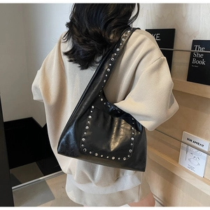 Détail d'un sac cabas en cuir noir à clous argentés porté par un mannequin en scène