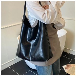Close-up of a glossy black leather tote bag worn by a model in a minimalist interior