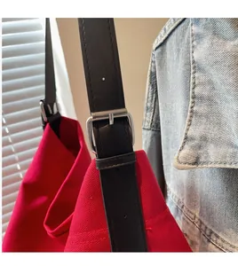 Detail of red canvas tote bag with adjustable black leather strap and silver metal buckle