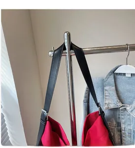 Detail of red canvas tote bag featuring black leather handles and silver metal adjusters
