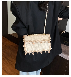 Detail shot of straw woven crossbody bag with shell tassels and golden chain strap