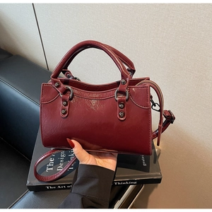 Detail einer dunkelroten glänzenden Handtasche mit Vintage-Nieten und zwei Griffen