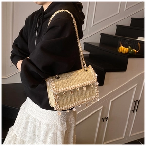 Detailed straw shoulder bag with seashell charms and metal chain strap on model