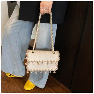 Detail of straw woven bag with shell pendants and gold metal chain strap on shoulder
