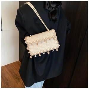 Detail of beige straw bag featuring seashell charms and golden chain strap on a black blazer