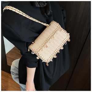 Detail of straw crossbody bag with natural weave, sea shells, and golden chain strap