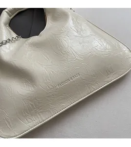Detail of cream pleated leather texture with embossed lettering and silver chain strap