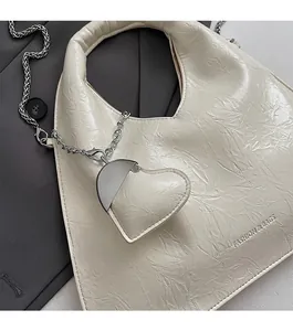 Detail of off-white pleated handbag featuring a heart charm and chain accessory