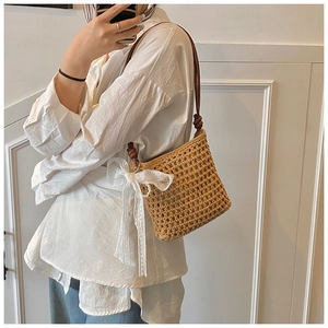 Détail du sac seau en paille tressée avec bandoulière en cuir et nœud en dentelle