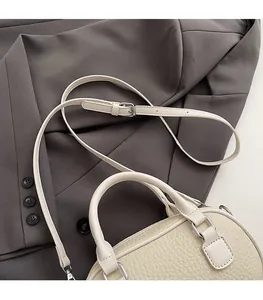Dettaglio ravvicinato di una borsa bowling in pelle crema con fibbie della tracolla