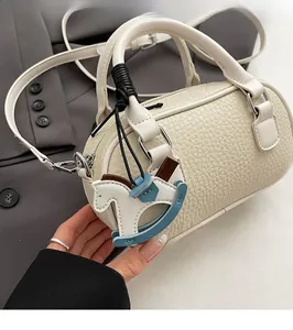 Dettaglio di una borsa Boston bianco crema con motivo litchi e ciondolo a cavallo a dondolo