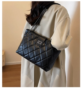Dettaglio borsa trapuntata nera con catena e chiusura in metallo su trench coat beige
