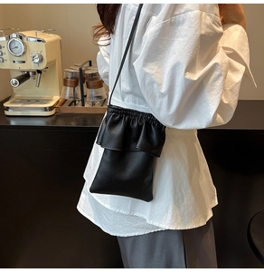 Détail d'un mini sac en cuir grainé noir avec des plis volantés dans un décor de café