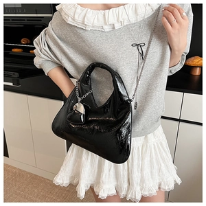 Detail of black patent leather bag with silver heart charm and metallic chain
